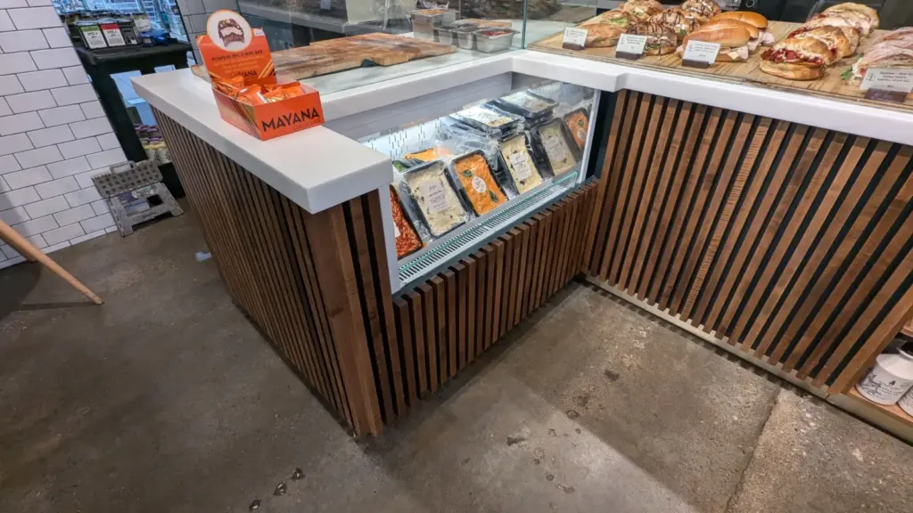 L-shaped service counter with white solid-surface top and stained wood slat cladding at Freebird Market, Toronto