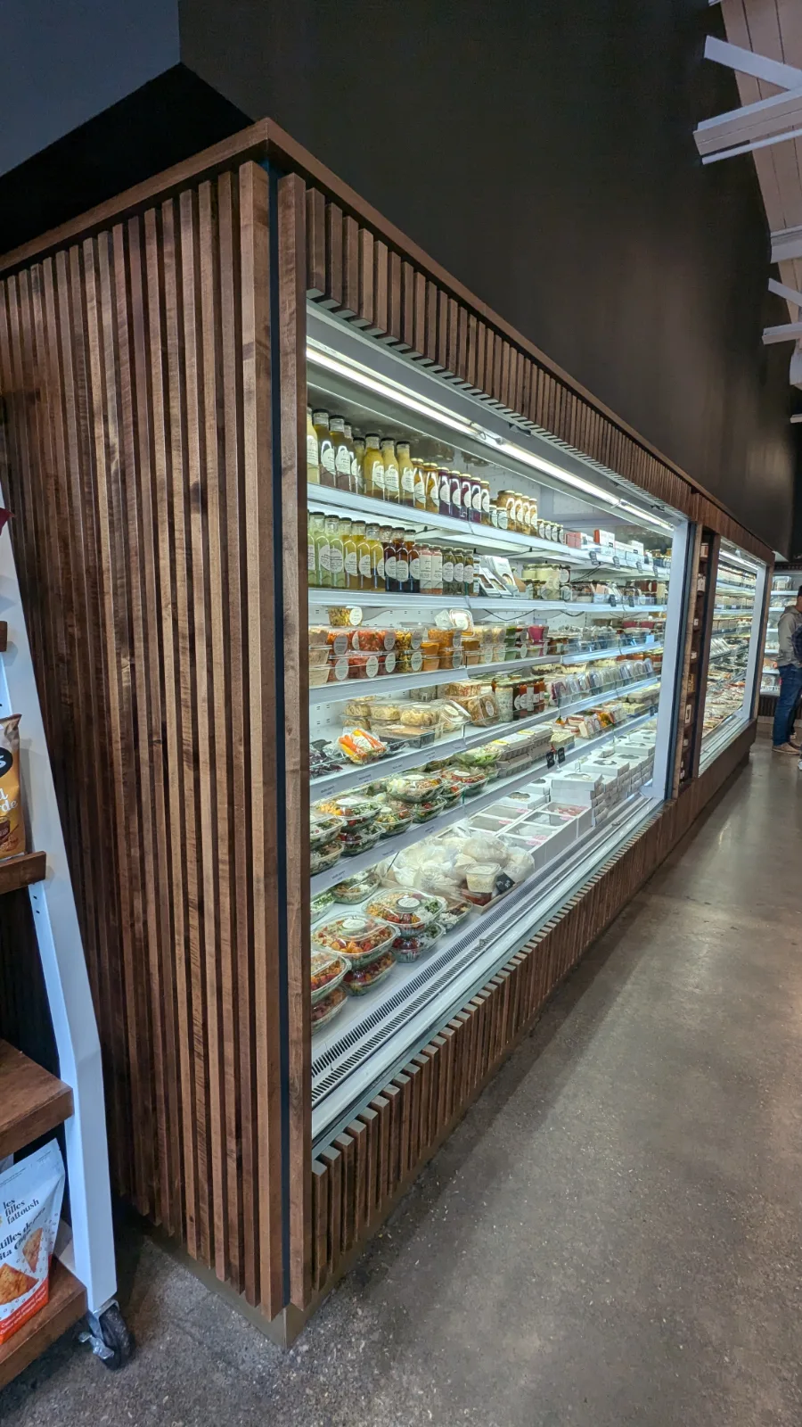 Refrigerated cases wrapped in a stained wood slat surround and canopy at Freebird Market, Toronto