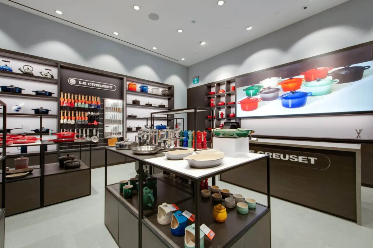 Le Creuset boutique with dark timber wall systems, glass-topped display tables and backlit product shelving.