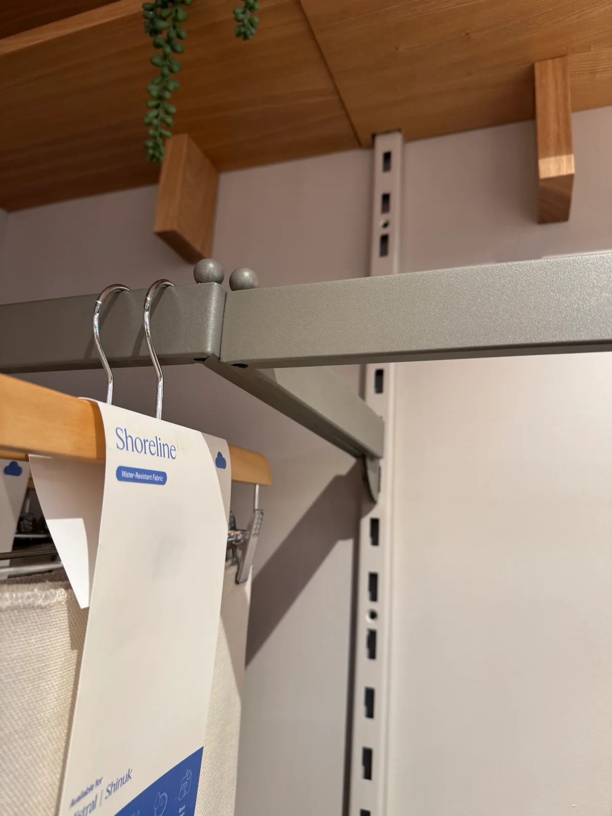 Slotted wall standard and powder-coated hang bar under an oak shelf in a furniture showroom