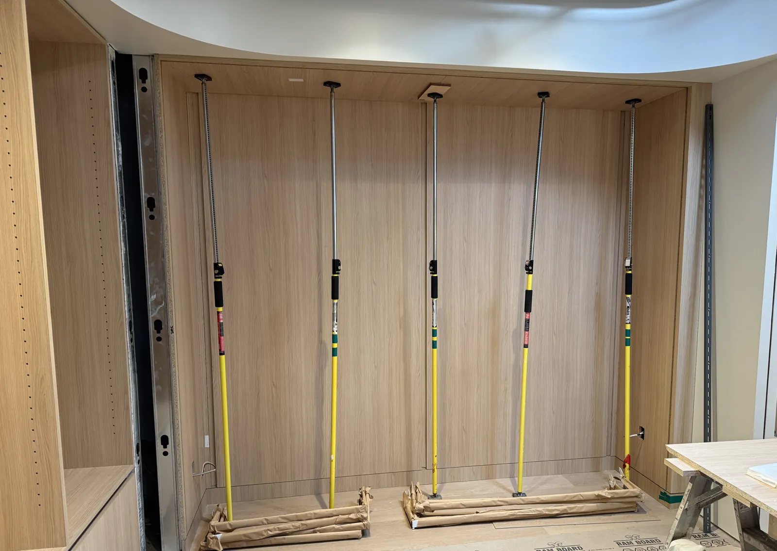 Oak wall panels being installed on metal hanging rails, with a wall standard at right, during a retail fit-out