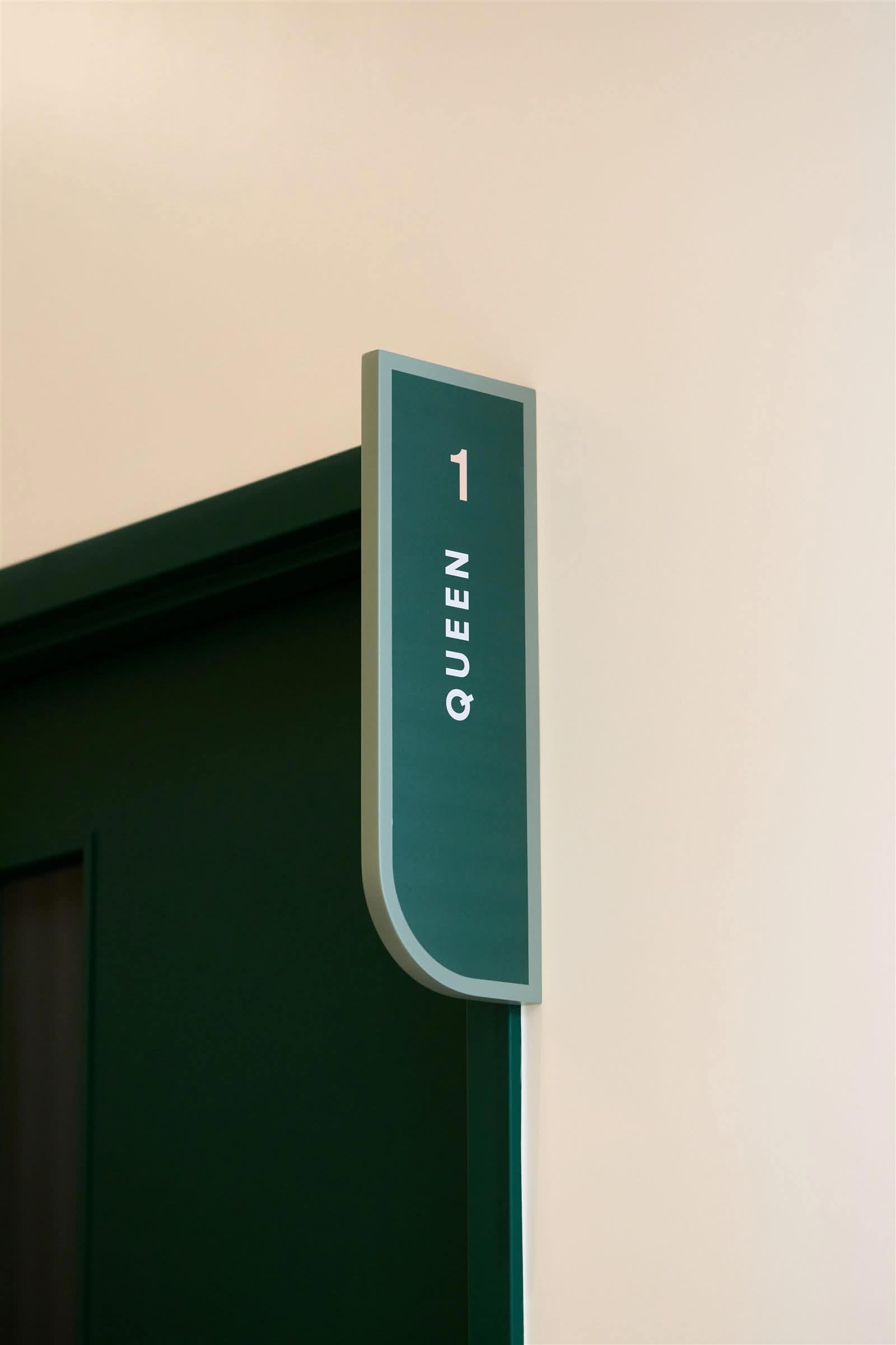 Green wayfinding blade sign marking exam room Queen 1 at Juno Veterinary