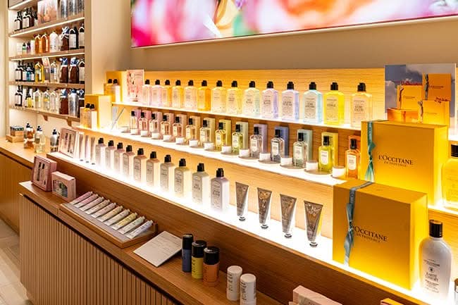 Tiered retail display shelving in oak with concealed LED strip lighting under every shelf, manufactured by DNS Industries for L’Occitane Park Royal, North Vancouver