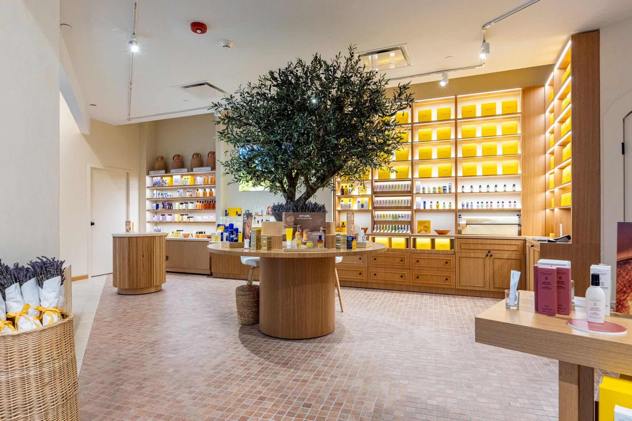 Curved fluted oak display plinths and a full-height illuminated shelving wall in an L’Occitane store at Plaza Las Américas, San Juan, Puerto Rico, manufactured by DNS Industries