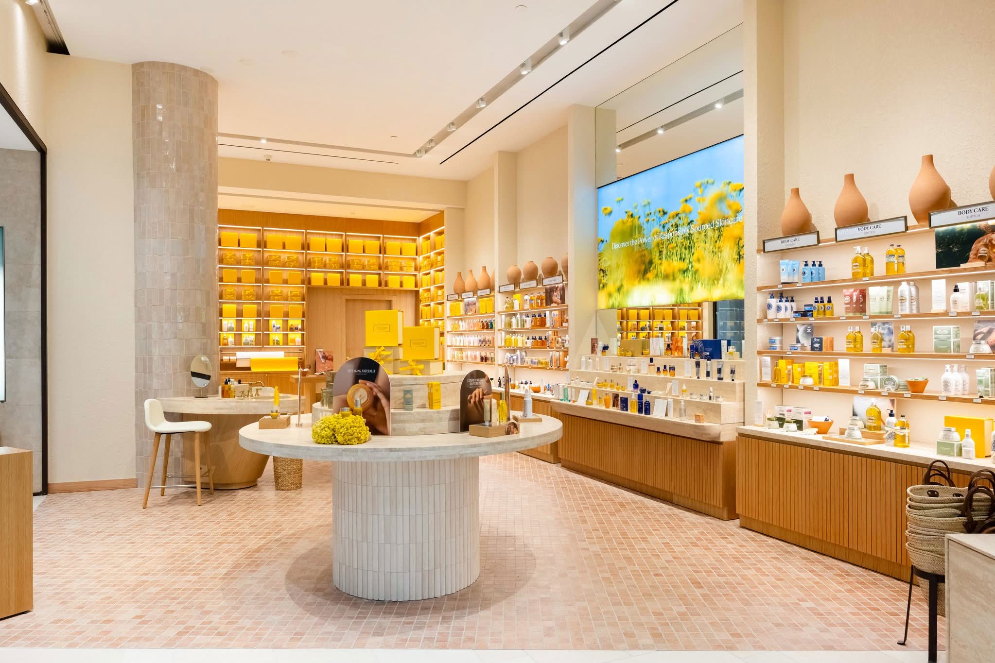 Interior of the L’Occitane en Provence store at Westfield Santa Anita, showing backlit product shelving, timber slat casework and a stone display island manufactured by DNS Industries
