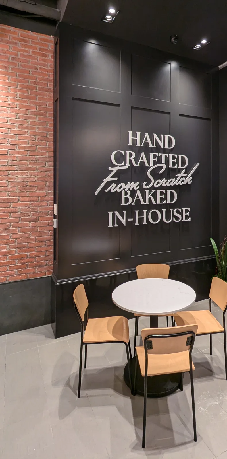 Black panelled feature wall with raised letters and a café table at Michel's Bakery Café, Yorkdale